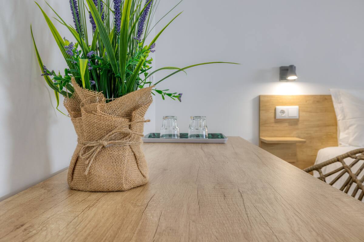 A wooden table with a burlap-wrapped vase containing green foliage and purple flowers.
