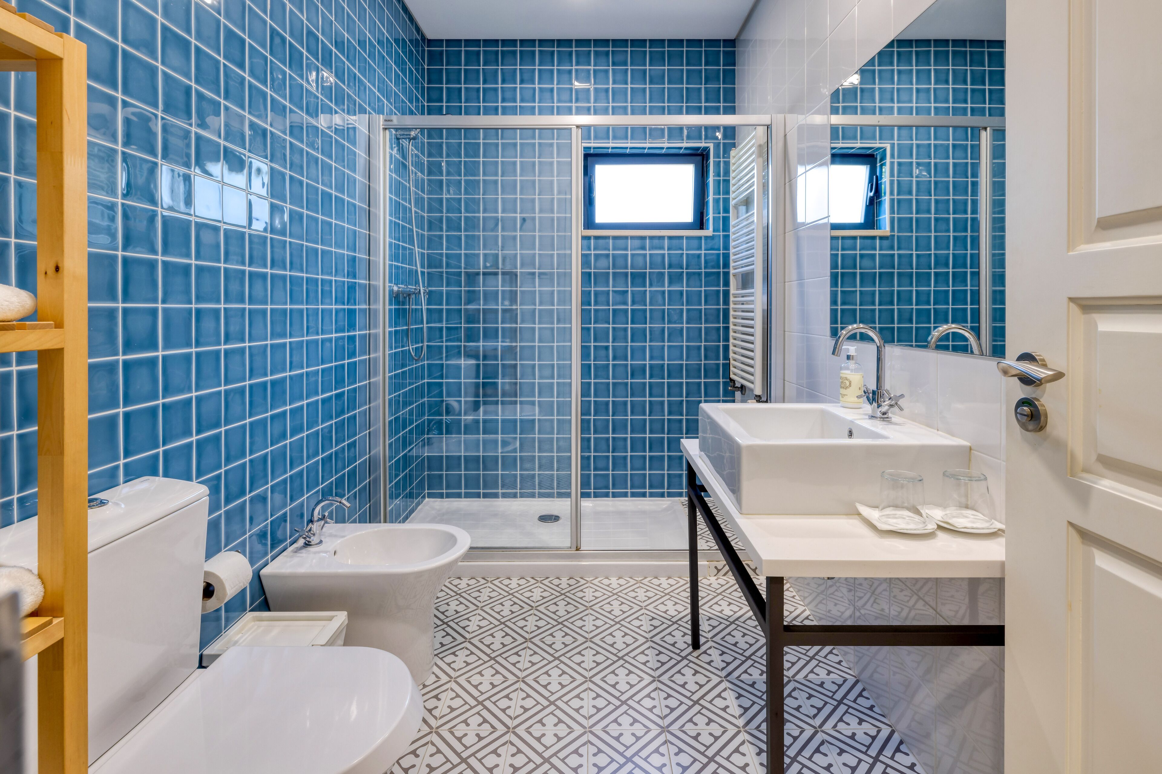 Un baño con paredes de azulejos azules, una ducha, un inodoro, un bidé y un lavabo con espejo.