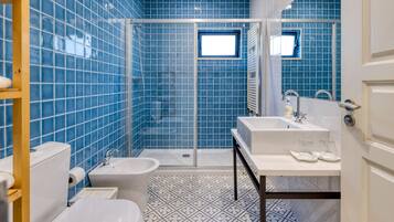 Un baño con paredes de azulejos azules, una ducha, un inodoro, un bidé y un lavabo con espejo.