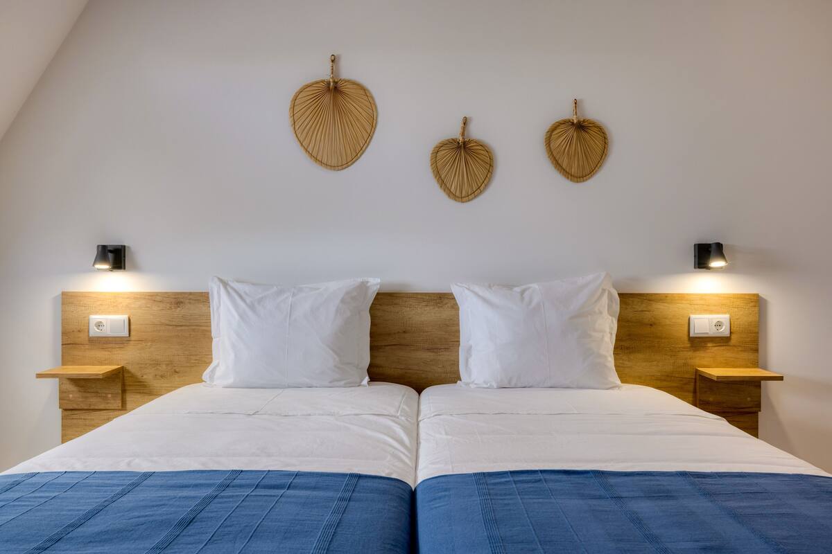 A double bed with white bedding, two bedside tables with lamps, and three wall-mounted decorative items.