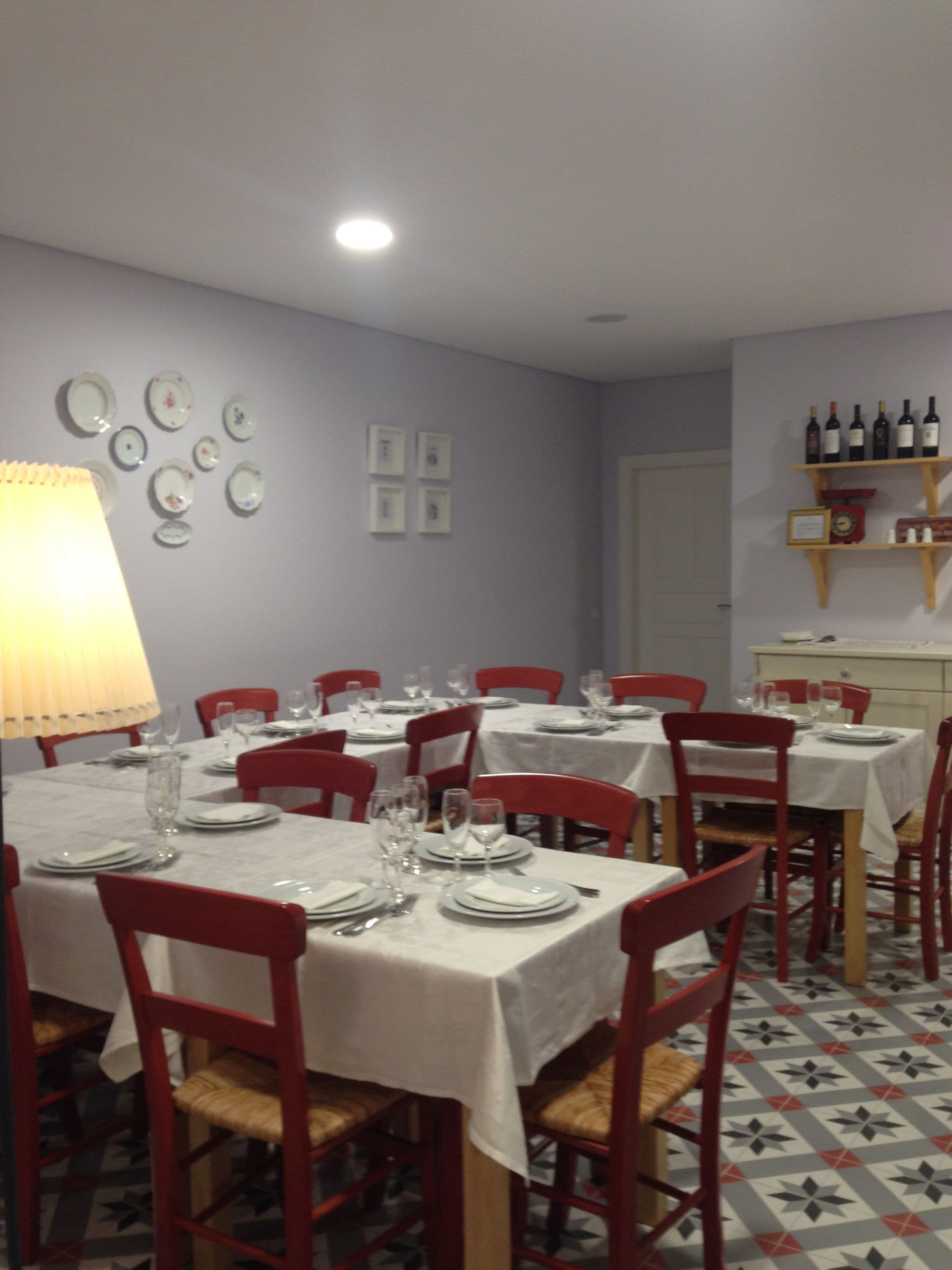 A dining area with tables set for six, red chairs, and a wall with framed pictures and a wine rack.