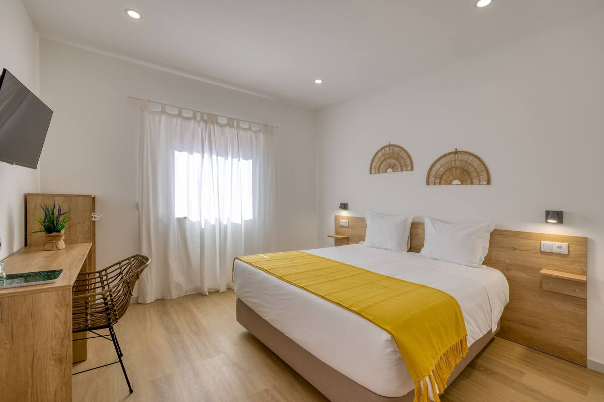 A modern hotel room with a bed, a desk, a chair, and a window with curtains.