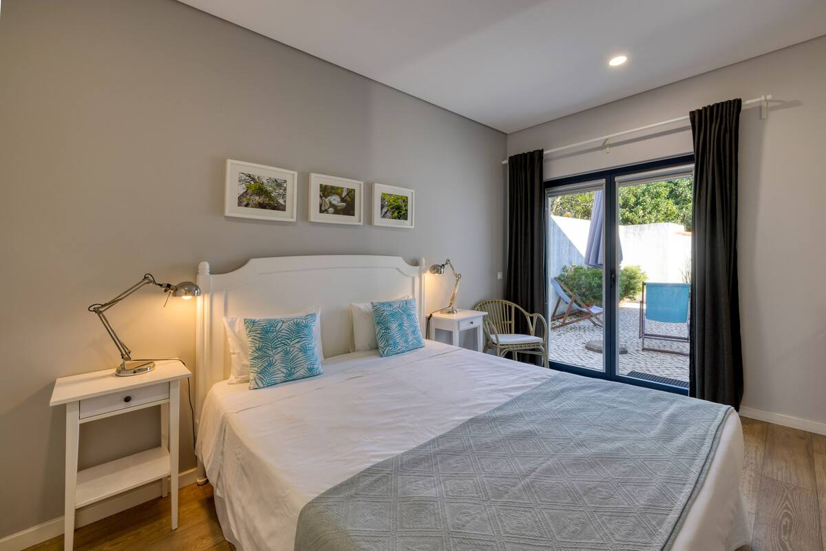 A bedroom with a bed, bedside tables, a desk, and a view of the outside.