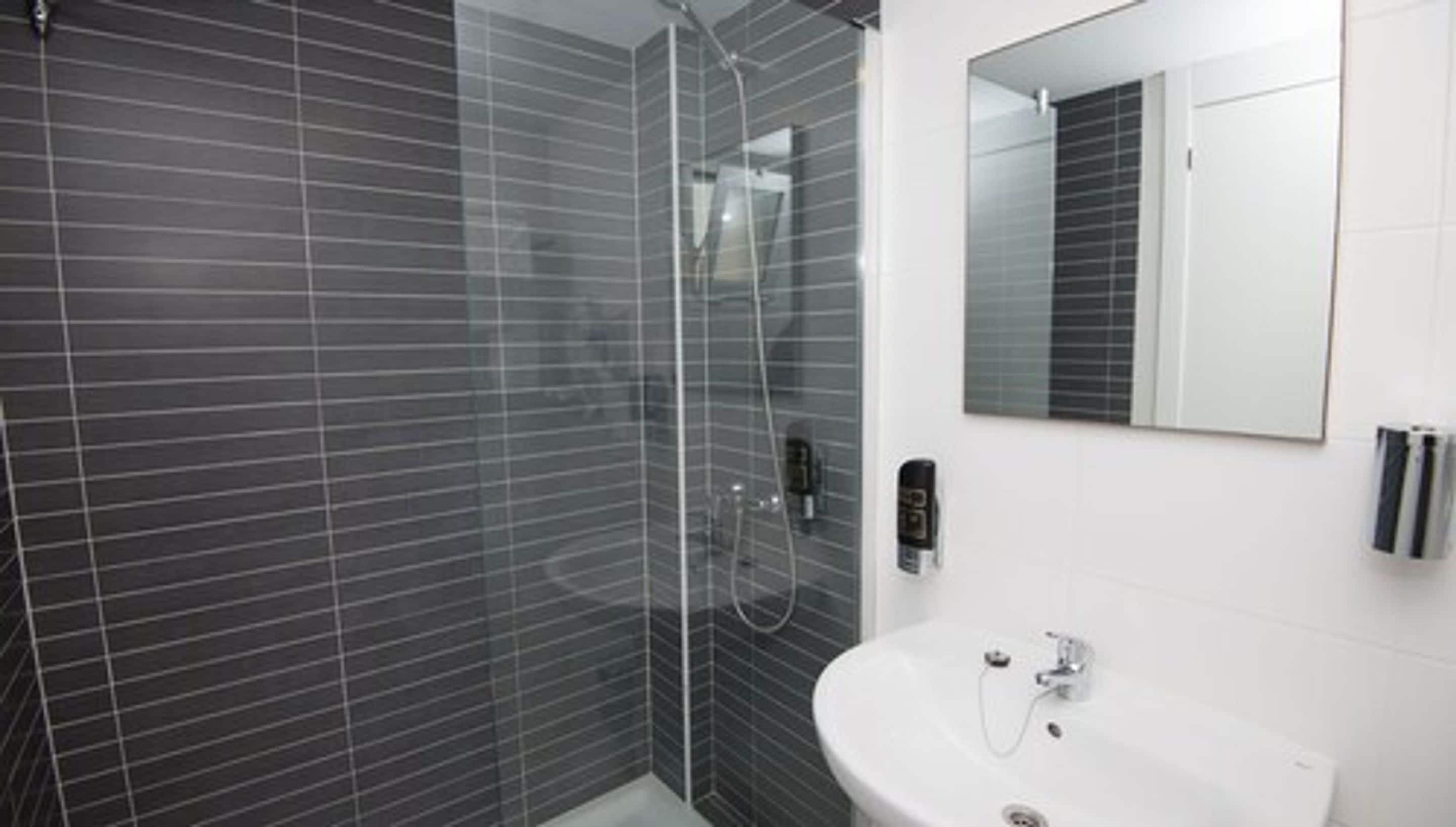 A modern bathroom with a glass-enclosed shower, a white sink, and a mirror above the sink.