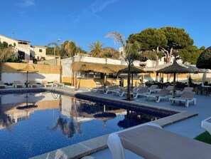 A pool area with lounge chairs and umbrellas, surrounded by buildings and trees.