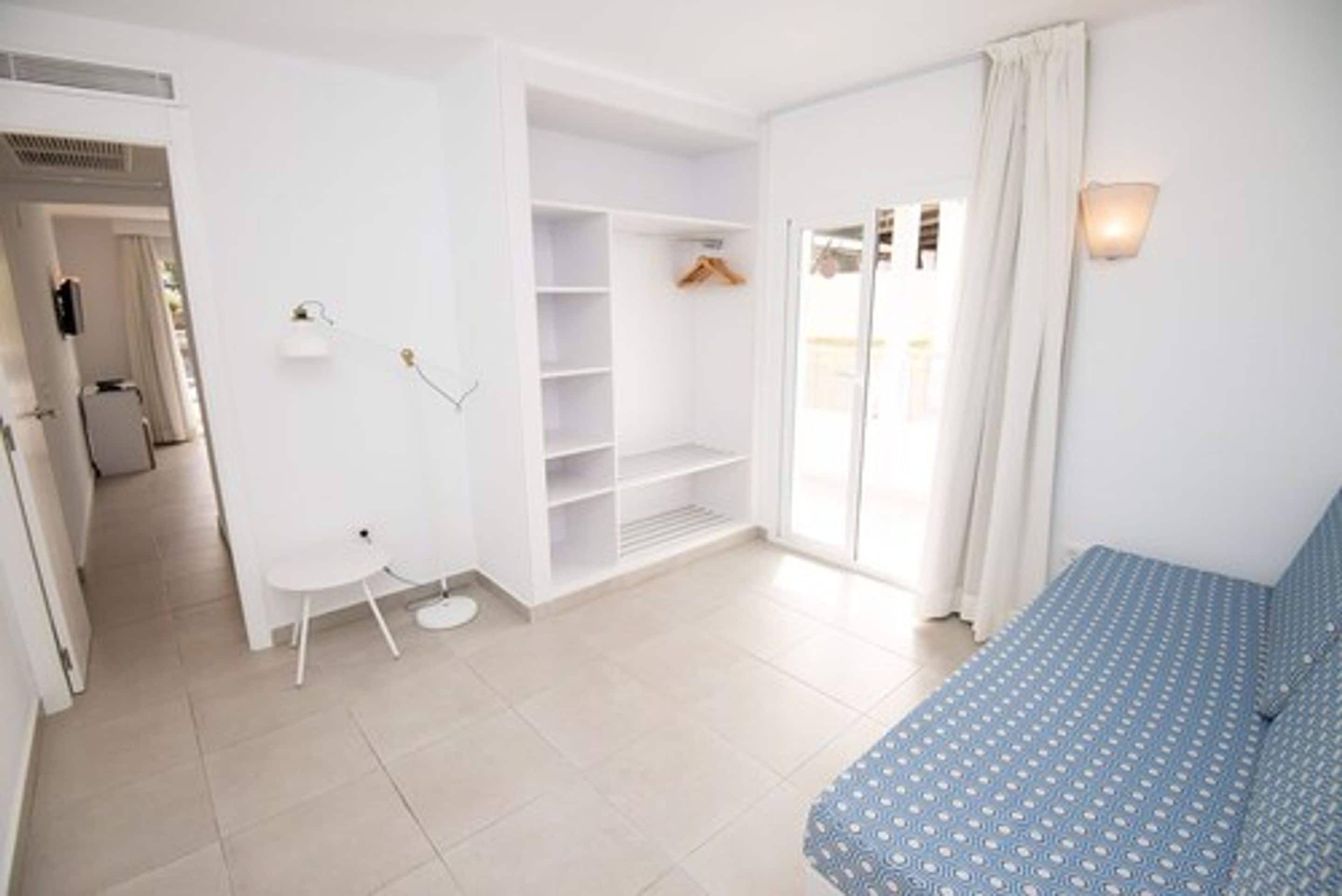 Una stanza con un letto, un tavolino, un armadio e una porta che dà su un balcone.