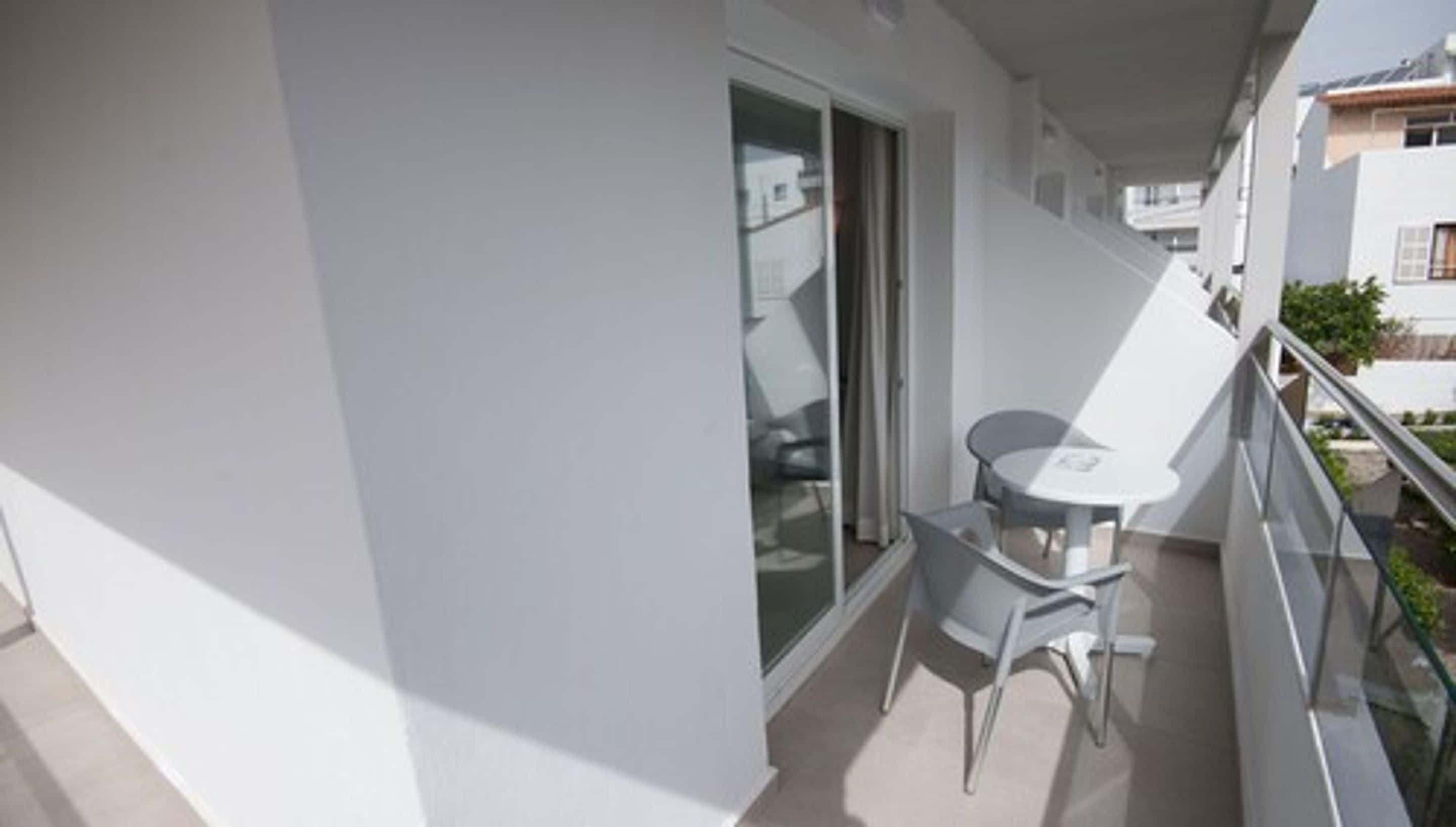A balcony with a table and chairs, a sliding glass door, and a view of neighboring buildings.