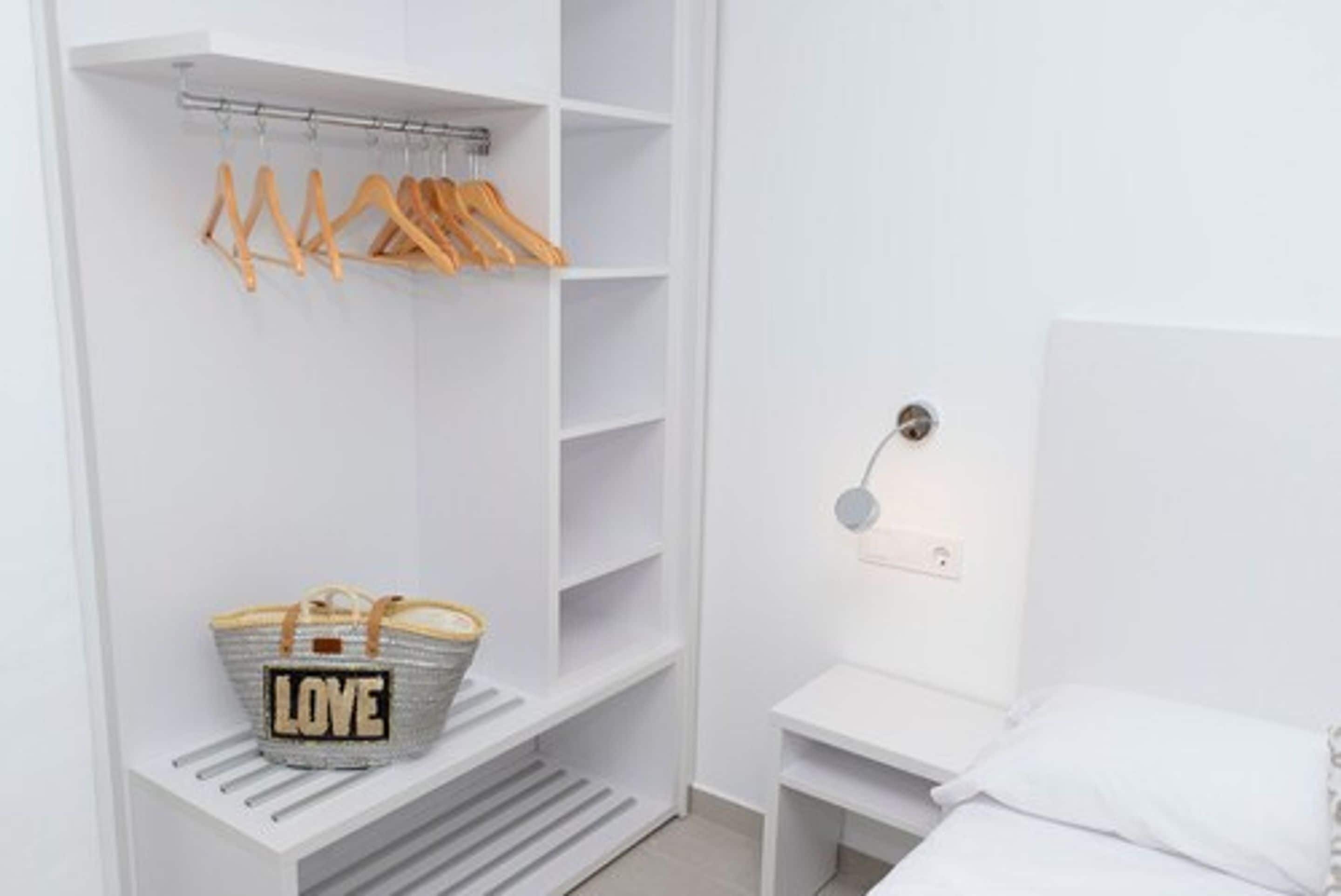 Un placard blanc avec des cintres en bois et un panier portant l’inscription « AMOUR » sur une étagère.