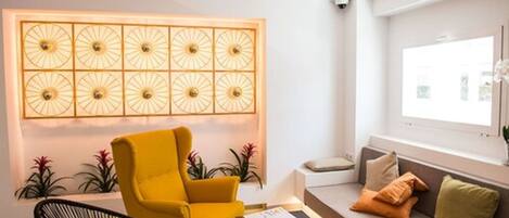 Een moderne woonkamer met een gele fauteuil, een bank met kussens, een salontafel en een decoratief wandpaneel.