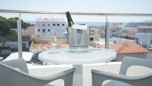 A balcony with a table, two chairs, a champagne bottle, and two glasses of champagne. - Hotel Chevy & Suites (Capdepera)