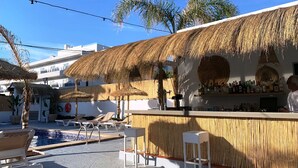 A bar area with a thatched roof, lounge chairs, and a pool. - Hotel Chevy & Suites (Capdepera)