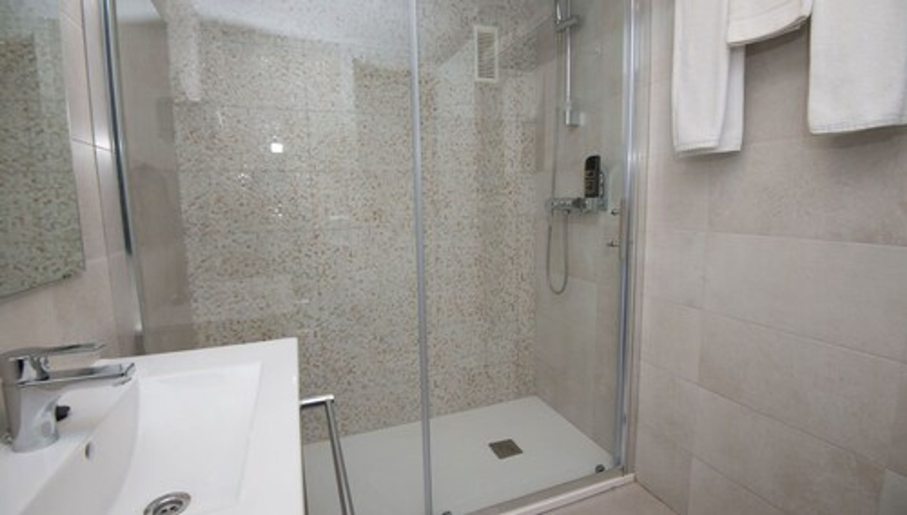 Un baño moderno con cabina de ducha de vidrio, lavamanos blanco y toallero.