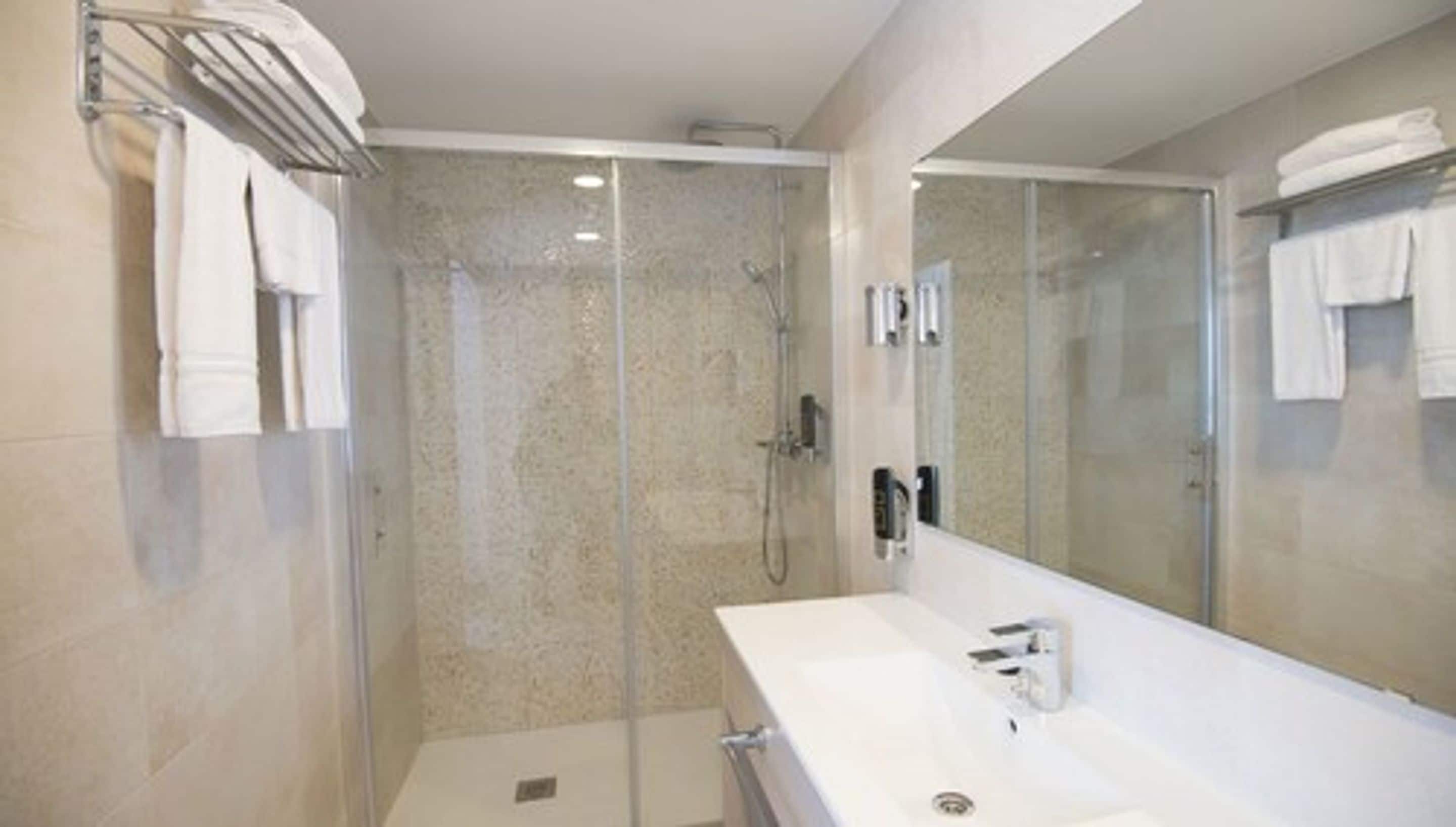 Une salle de bain moderne avec une douche à parois de verre, un lavabo blanc et un grand miroir.