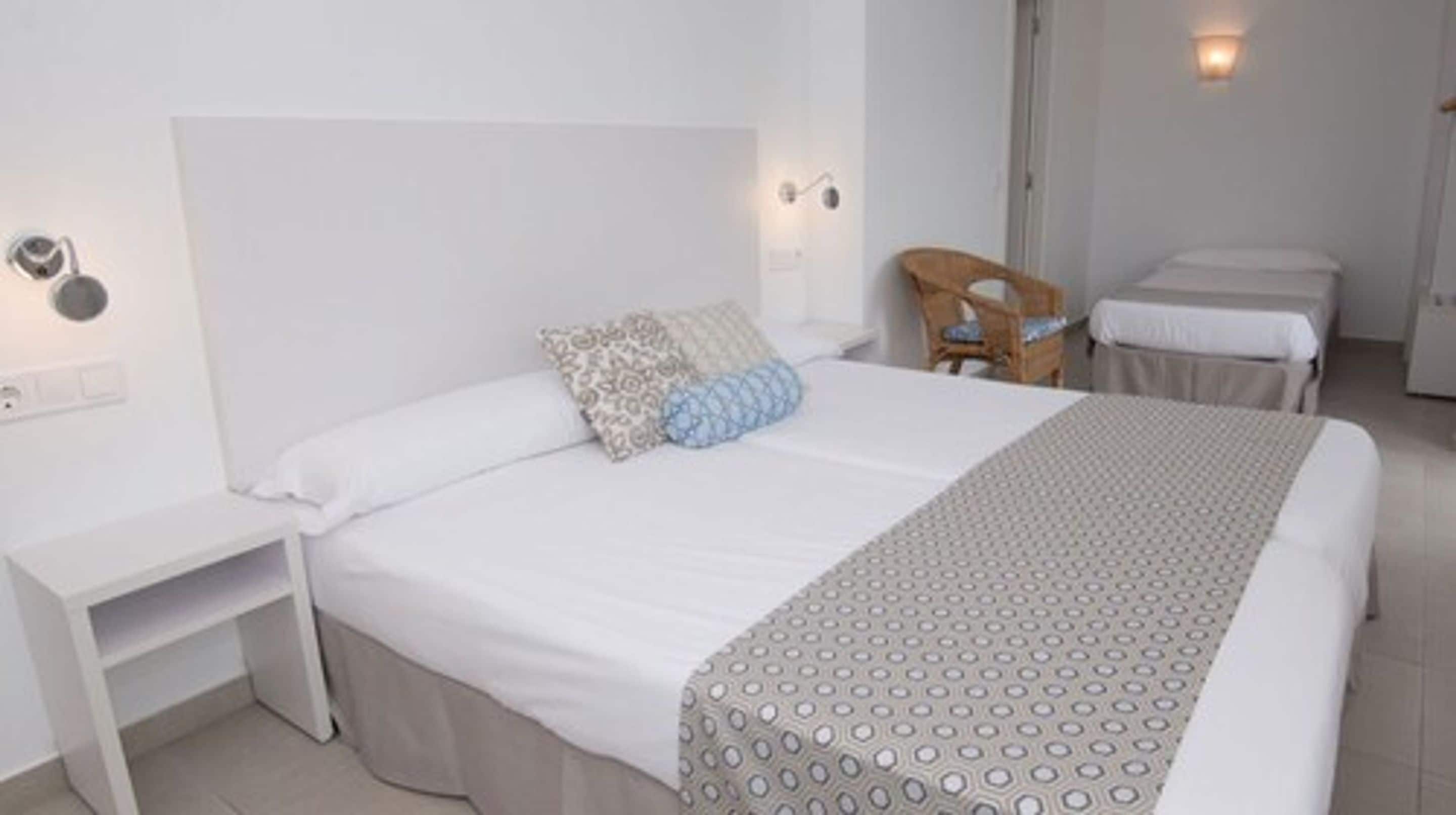 A hotel room with a large bed, a bedside table, a chair, and a small table.