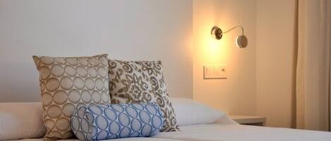 A neatly made bed with patterned pillows, a wall-mounted light fixture, and a plain wall.