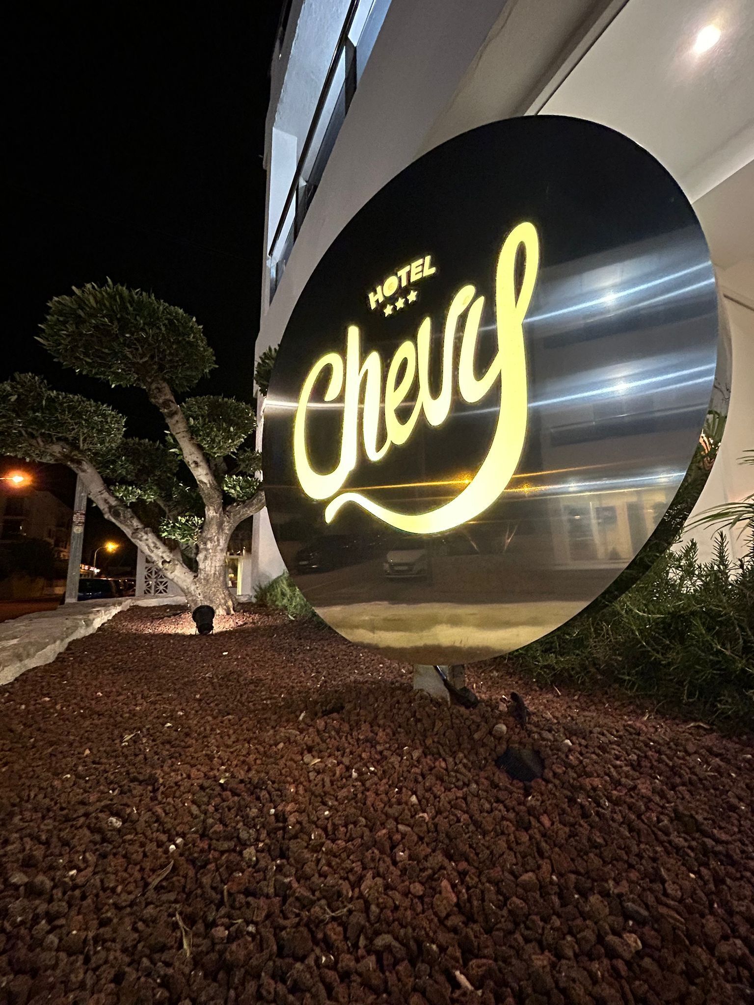 A hotel sign with the name 'Hotel Chevas' illuminated at night.