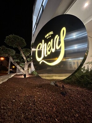 A hotel sign with the name 'Hotel Chevas' illuminated at night.