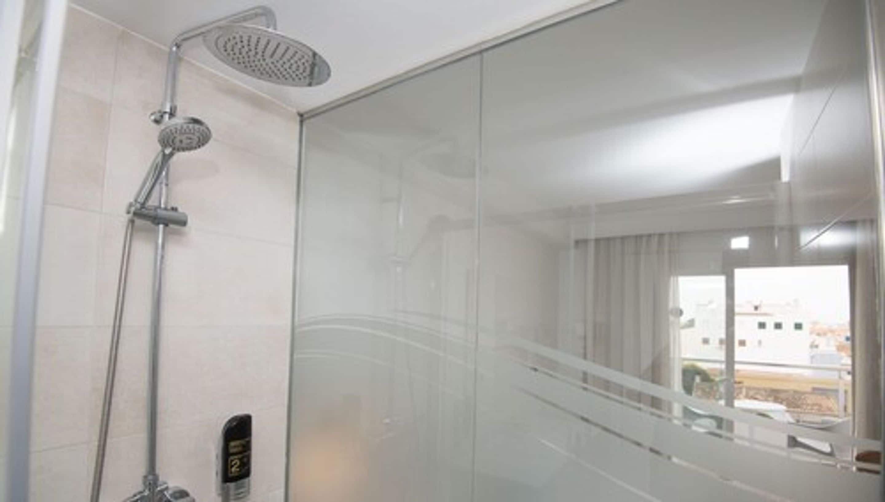 A modern bathroom with a glass shower enclosure, a handheld showerhead, and a control panel.