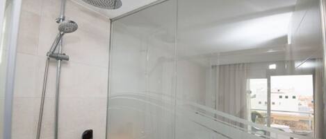 A modern bathroom with a glass shower enclosure, a handheld showerhead, and a control panel.