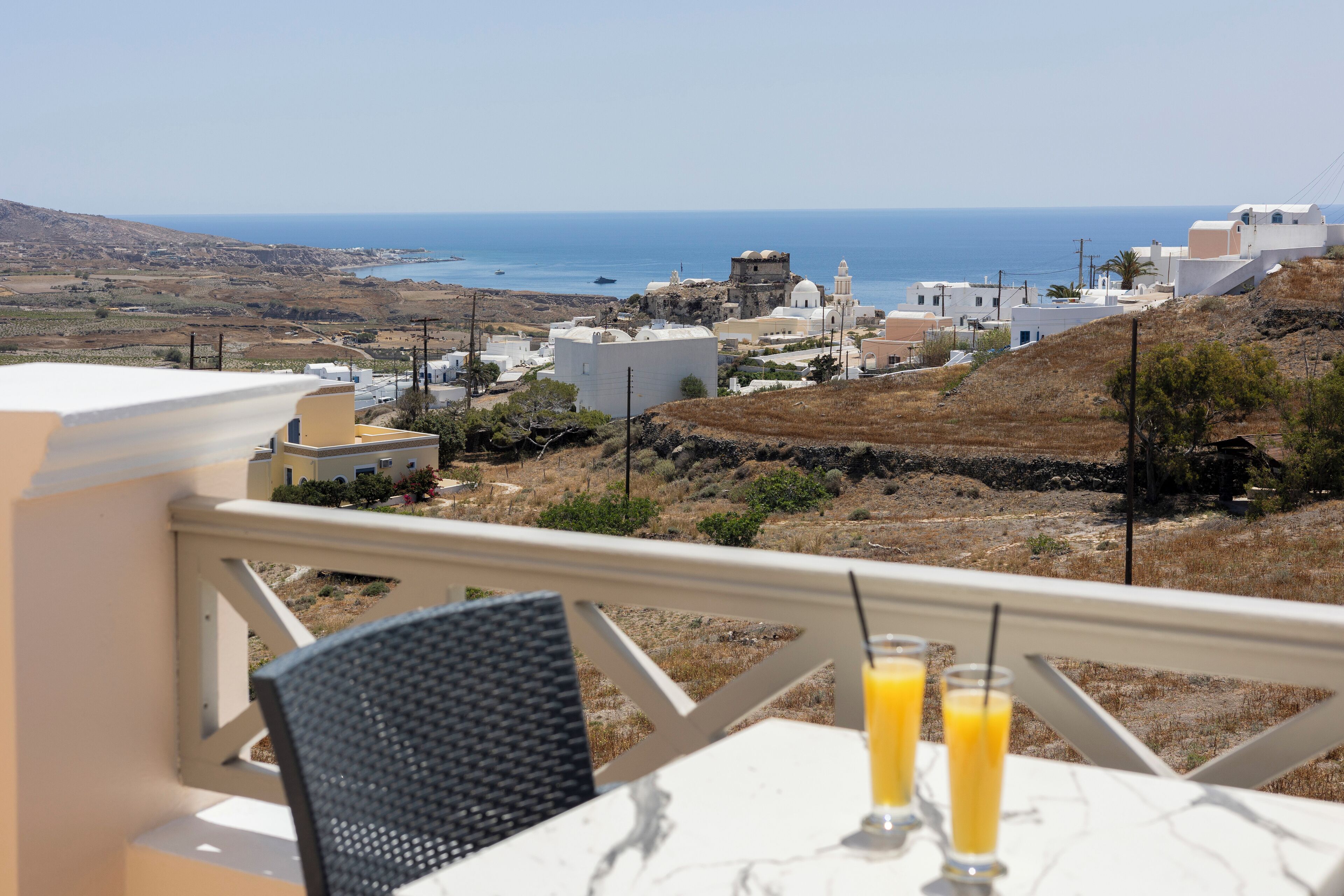 Una terraza con mesa y sillas, con vista a un pueblo costero, edificios y el mar.