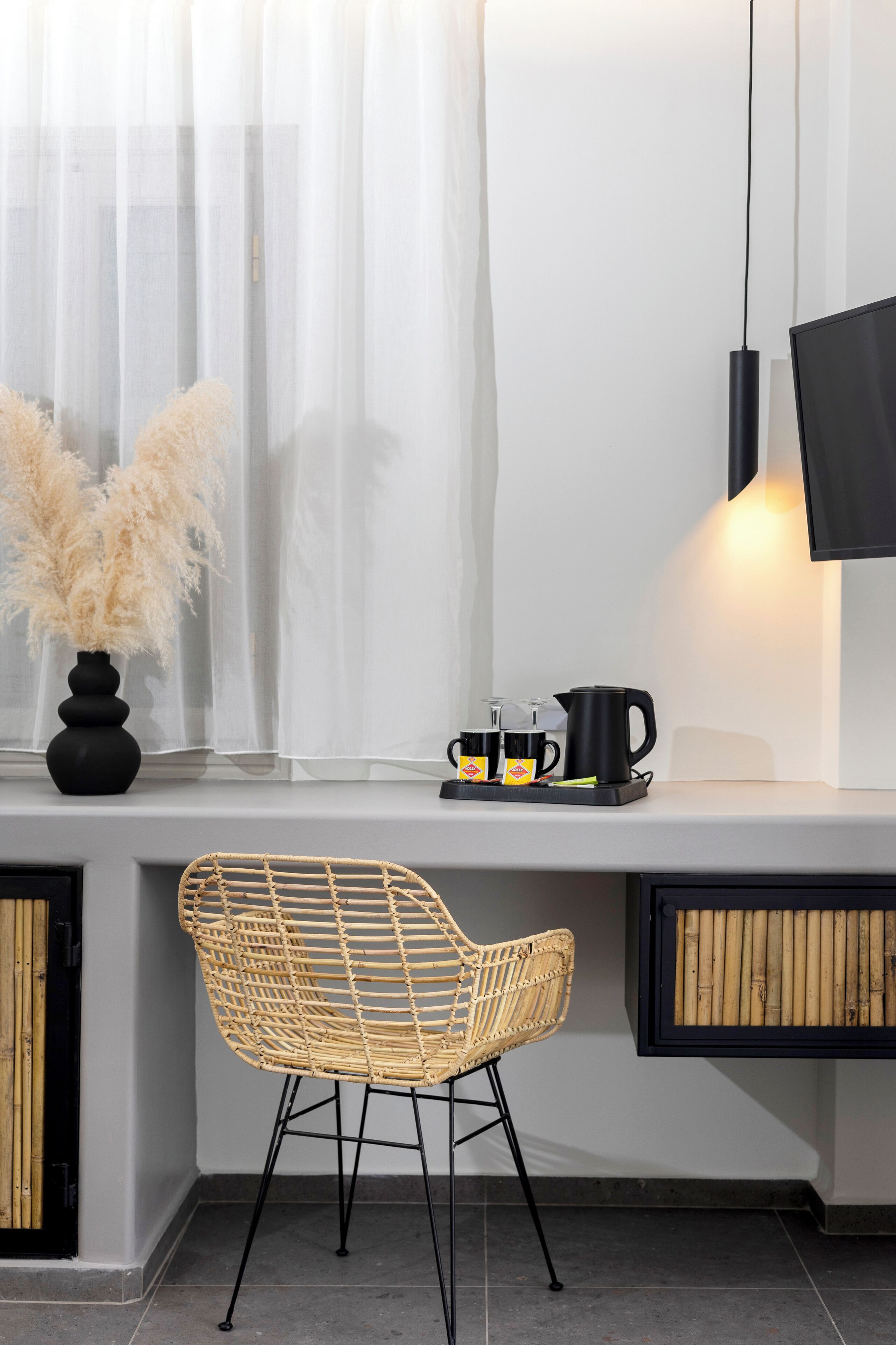A modern kitchen with a built-in bench, a wicker chair, a coffee station, and a flat-screen TV mounted on the wall.