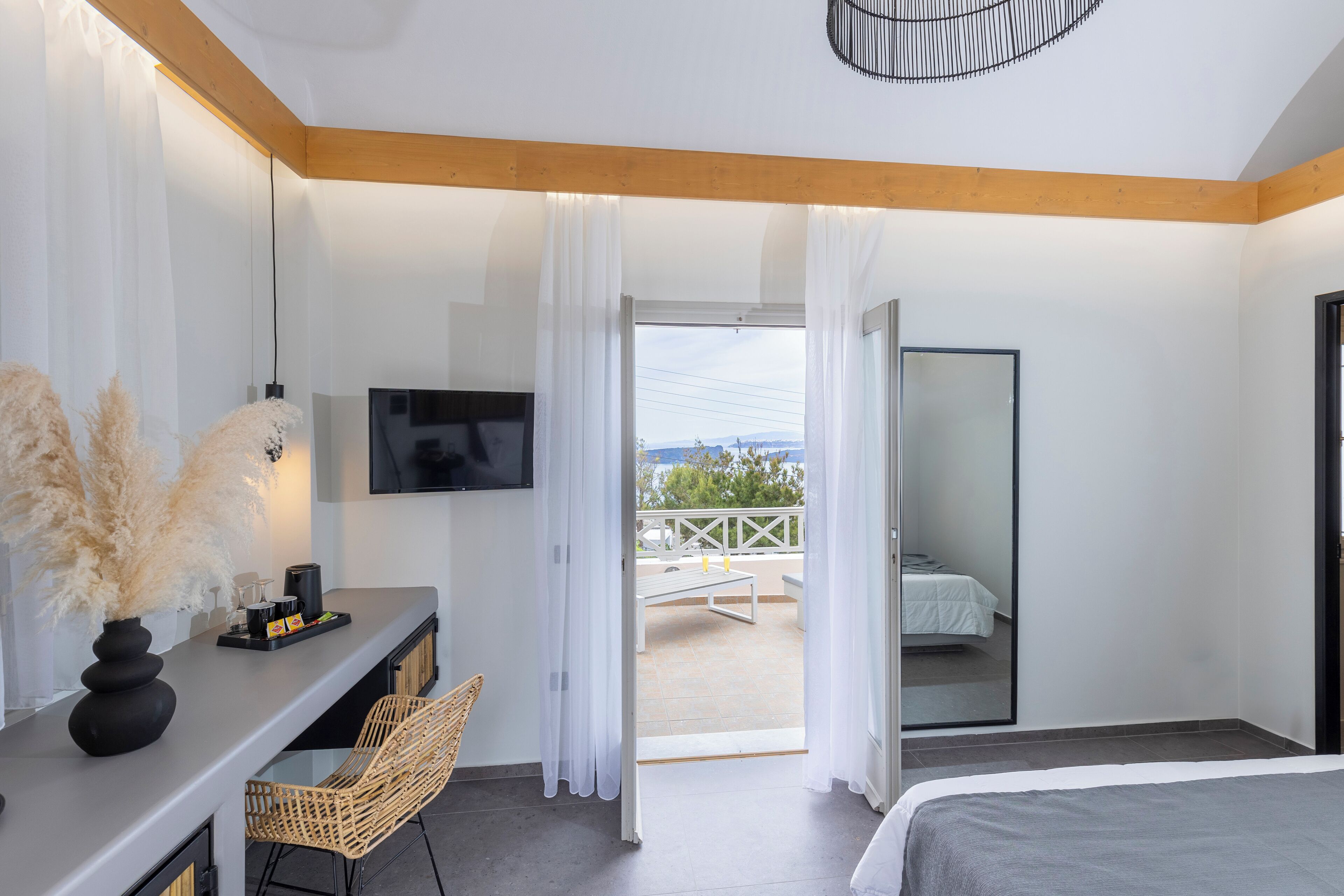 Una habitación de hotel moderna con una cama, un escritorio con televisor, un balcón con vistas y un área de comedor con mesa y sillas.
