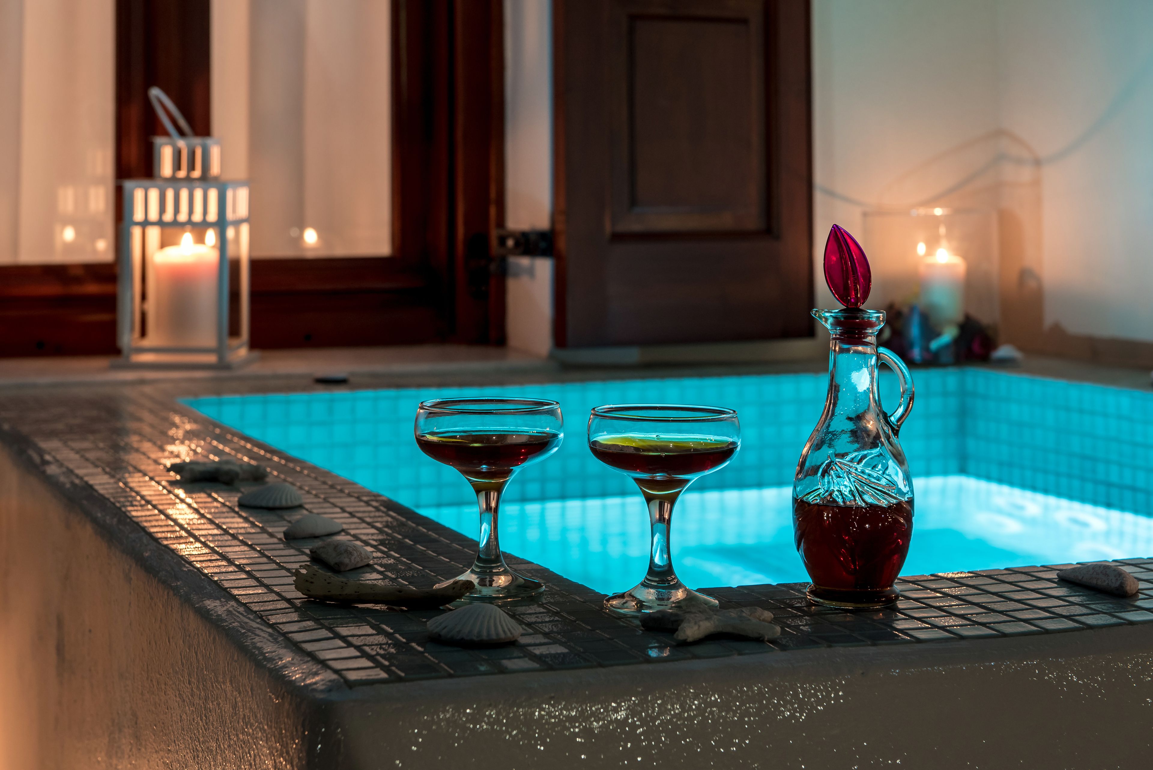 Zona junto a la piscina con dos vasos de bebida y una jarra, rodeada de conchas marinas y una vela.