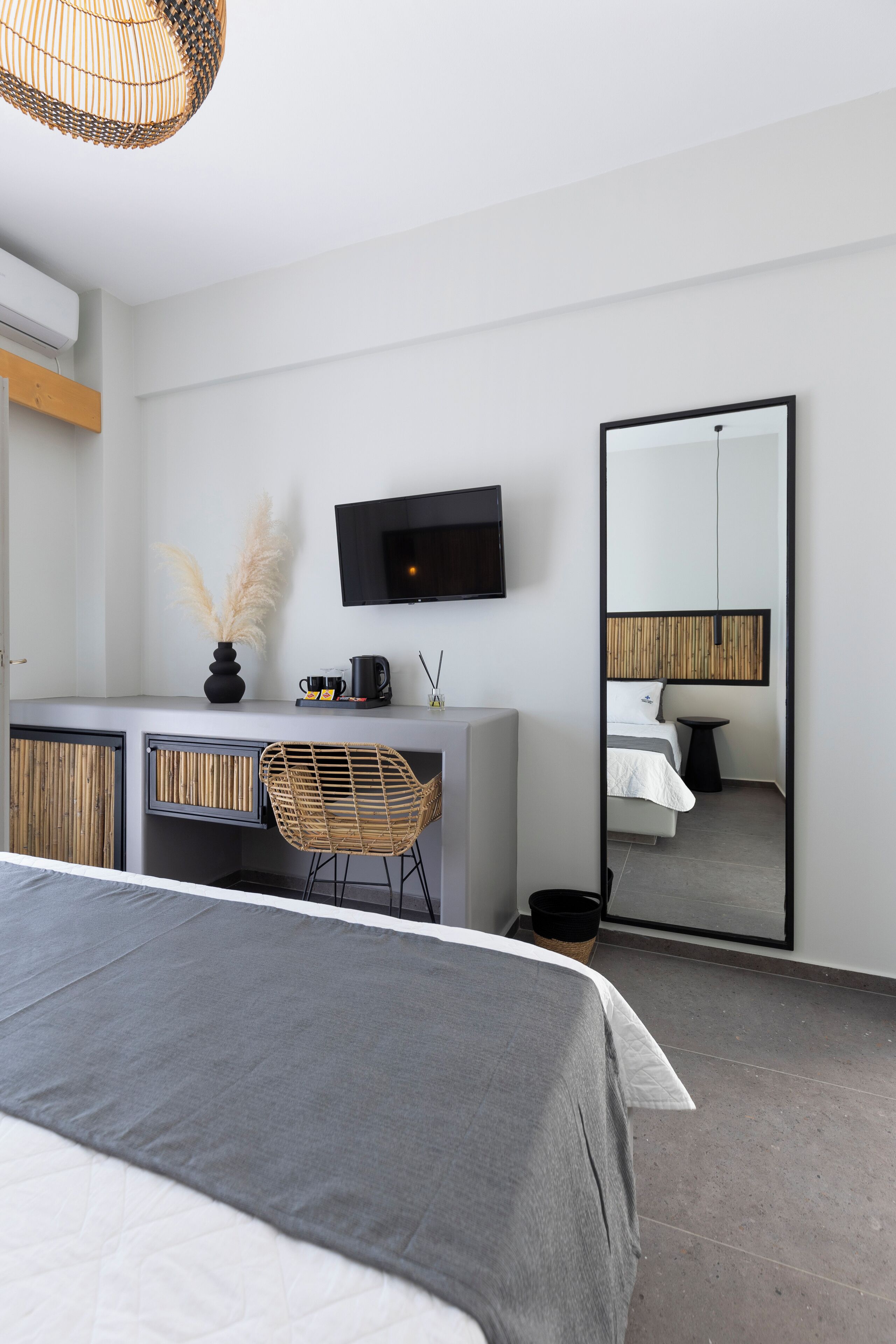 A modern hotel room with a bed, a desk with a chair, a television, and a large mirror.
