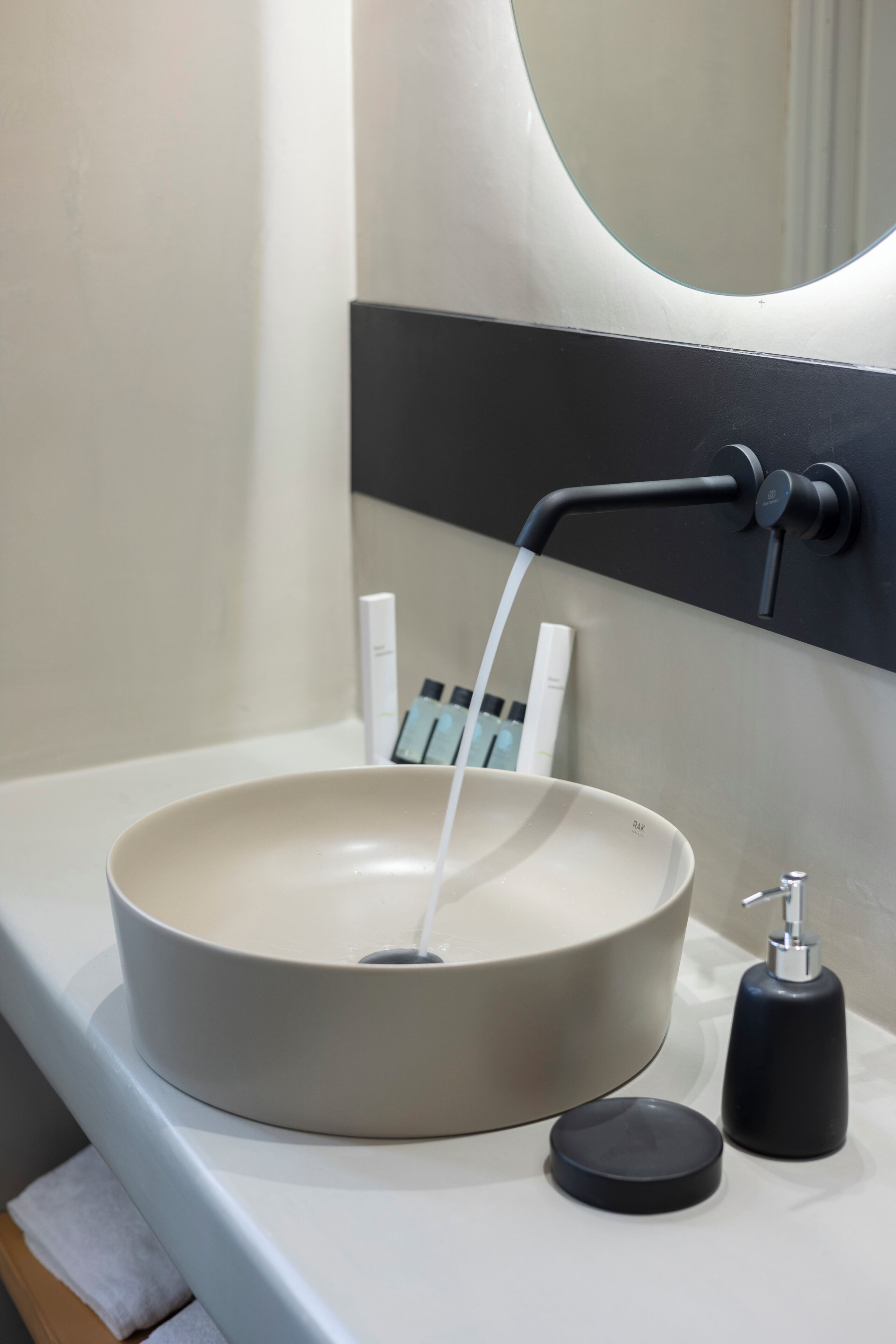 Ein modernes Badezimmer mit einem runden, beigefarbenen Waschbecken, einem schwarzen Wasserhahn, einem Spiegel und einer Seifenspender.