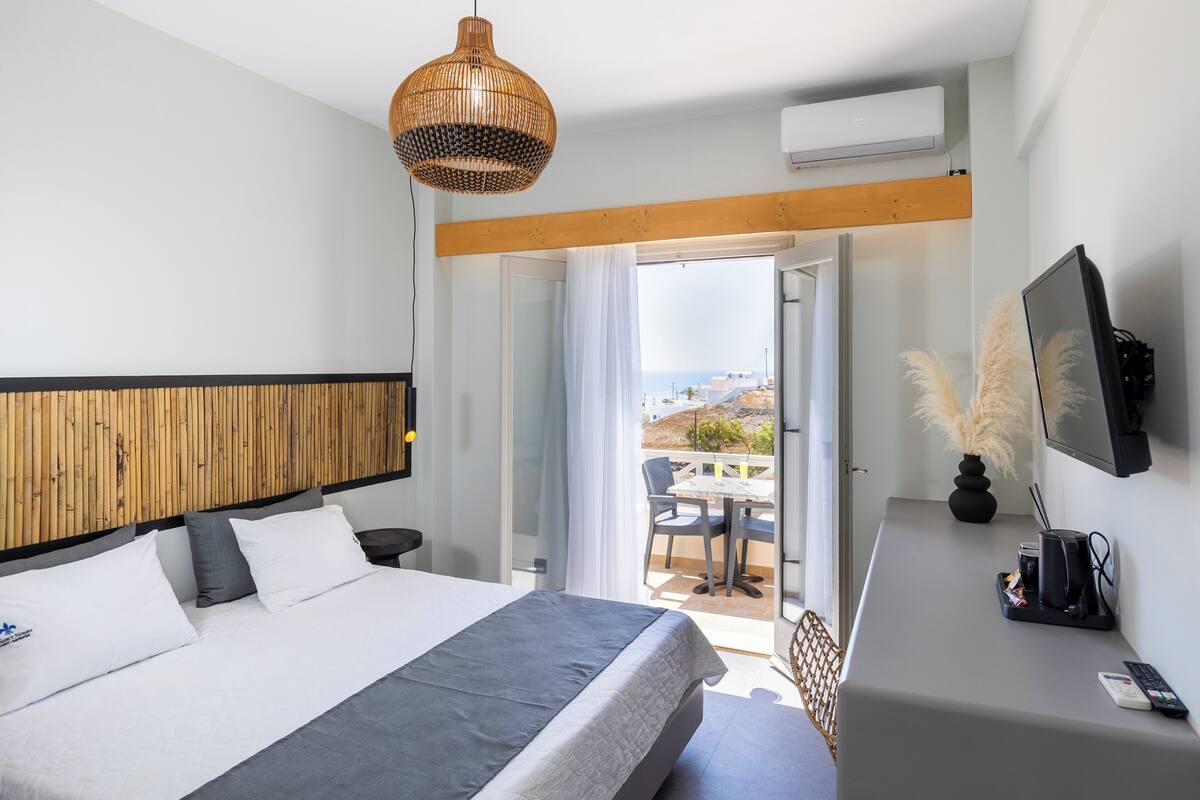 A modern hotel room with a bed, a desk, and a view of the sea.
