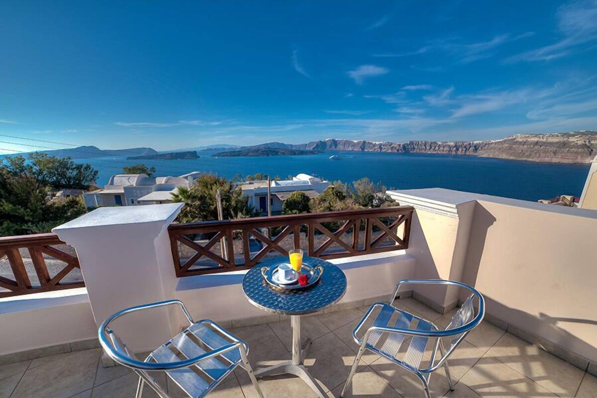 A terrace with two metal chairs and a small round table, overlooking a coastal landscape with clear skies.