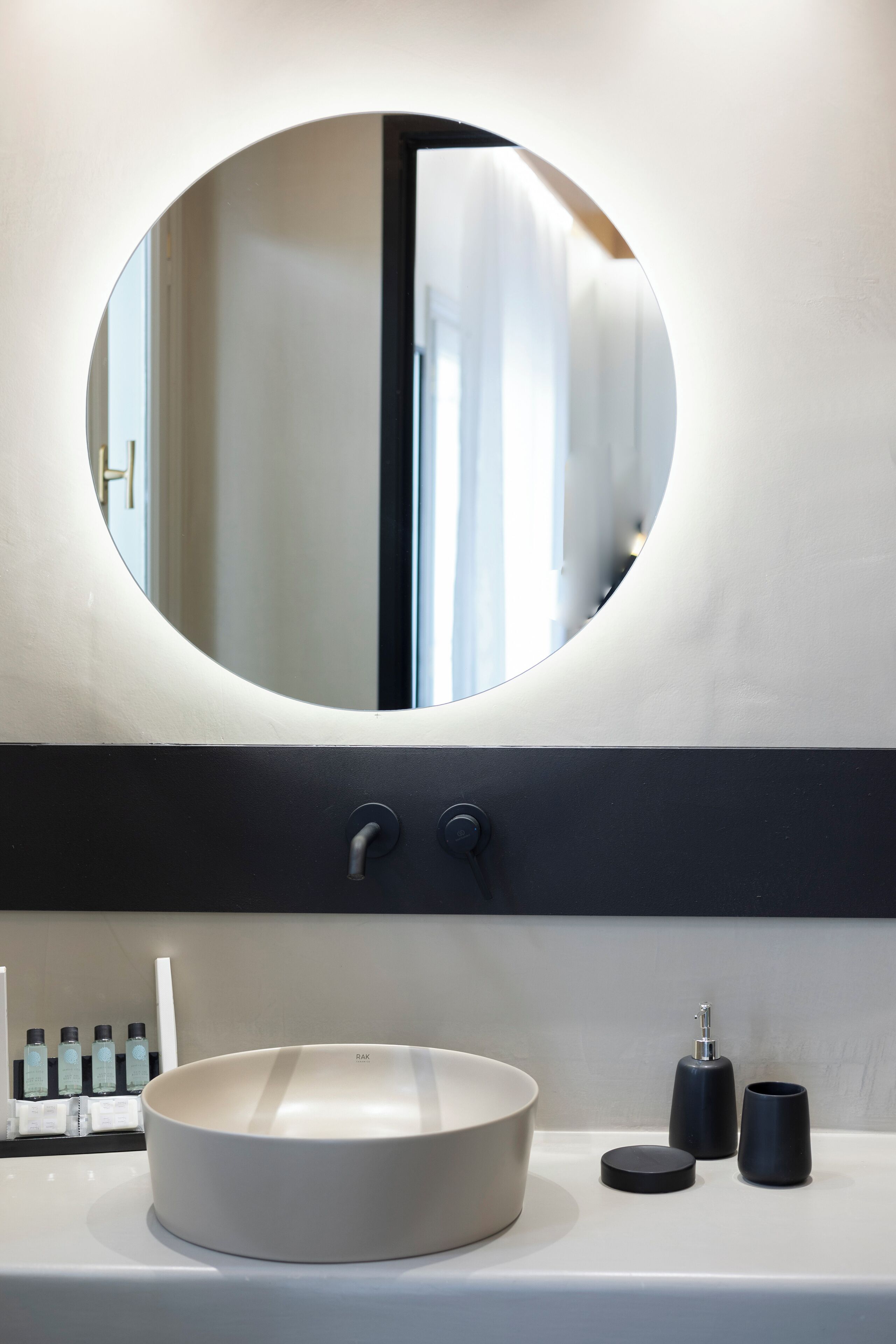 A bathroom with a round mirror, a white sink, and two black containers.