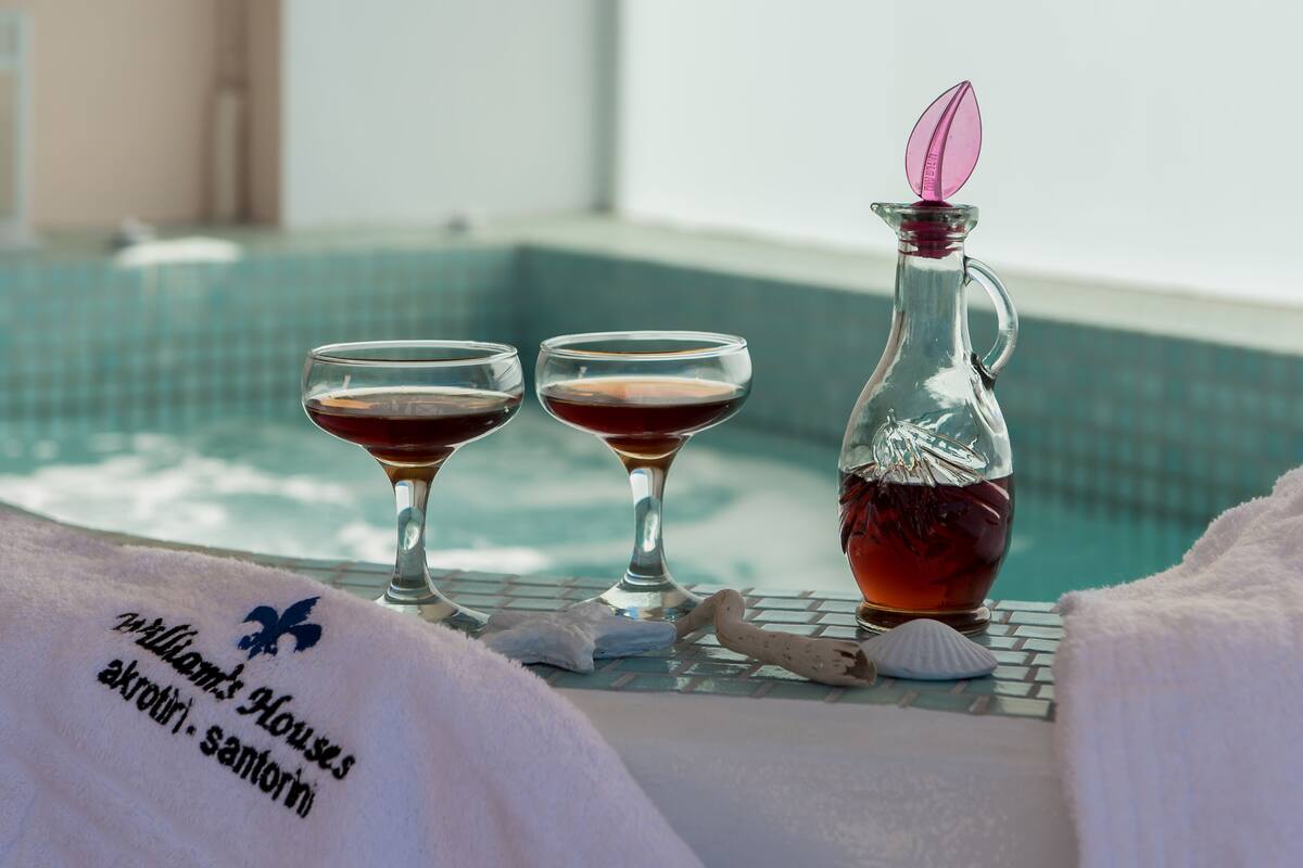 A poolside setting with two glasses of red beverage, a clear bottle with a pink flower, and a towel with text.