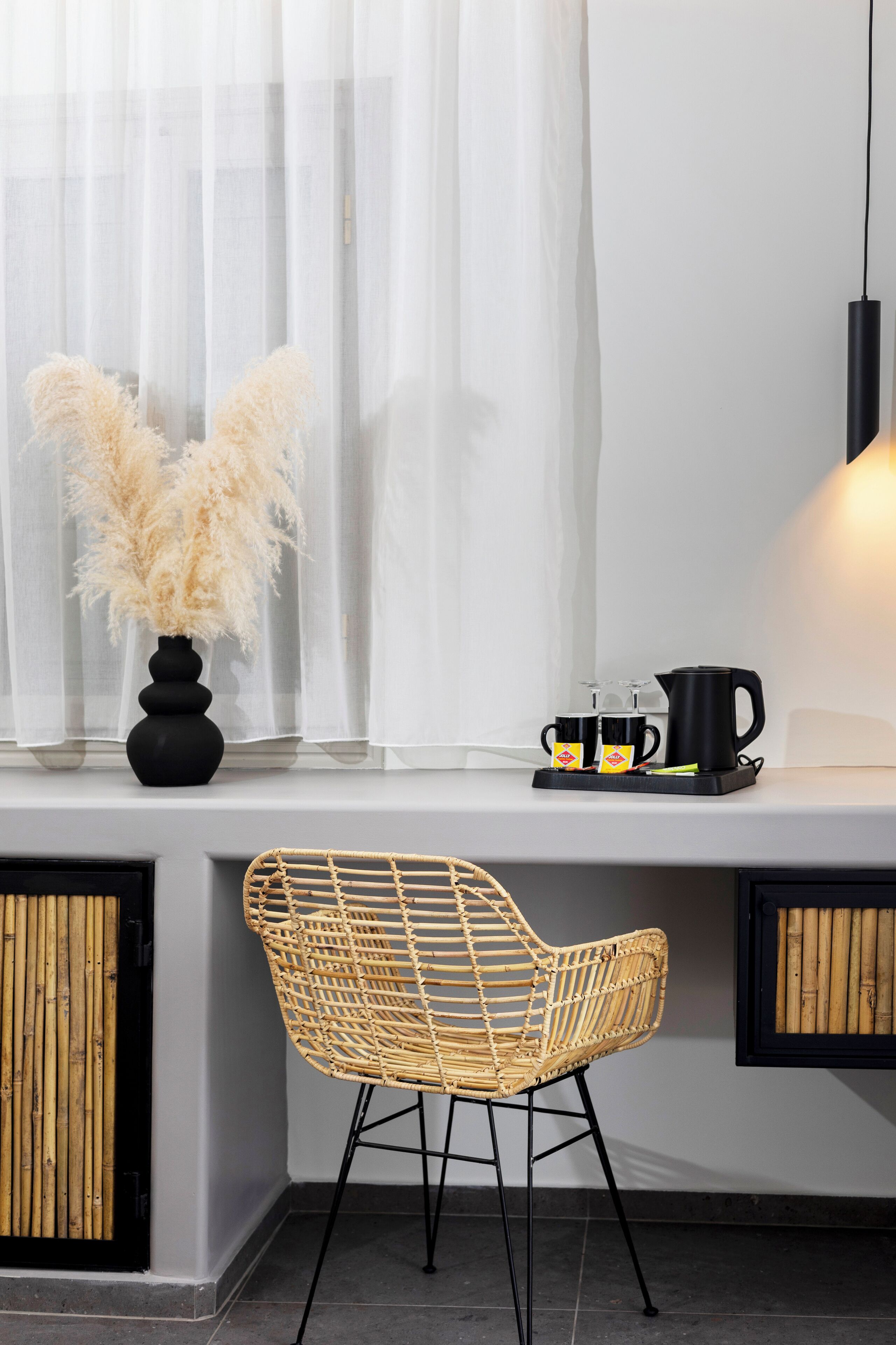A modern room with a wicker chair, a black vase with pampas grass, and a coffee setup on a windowsill.