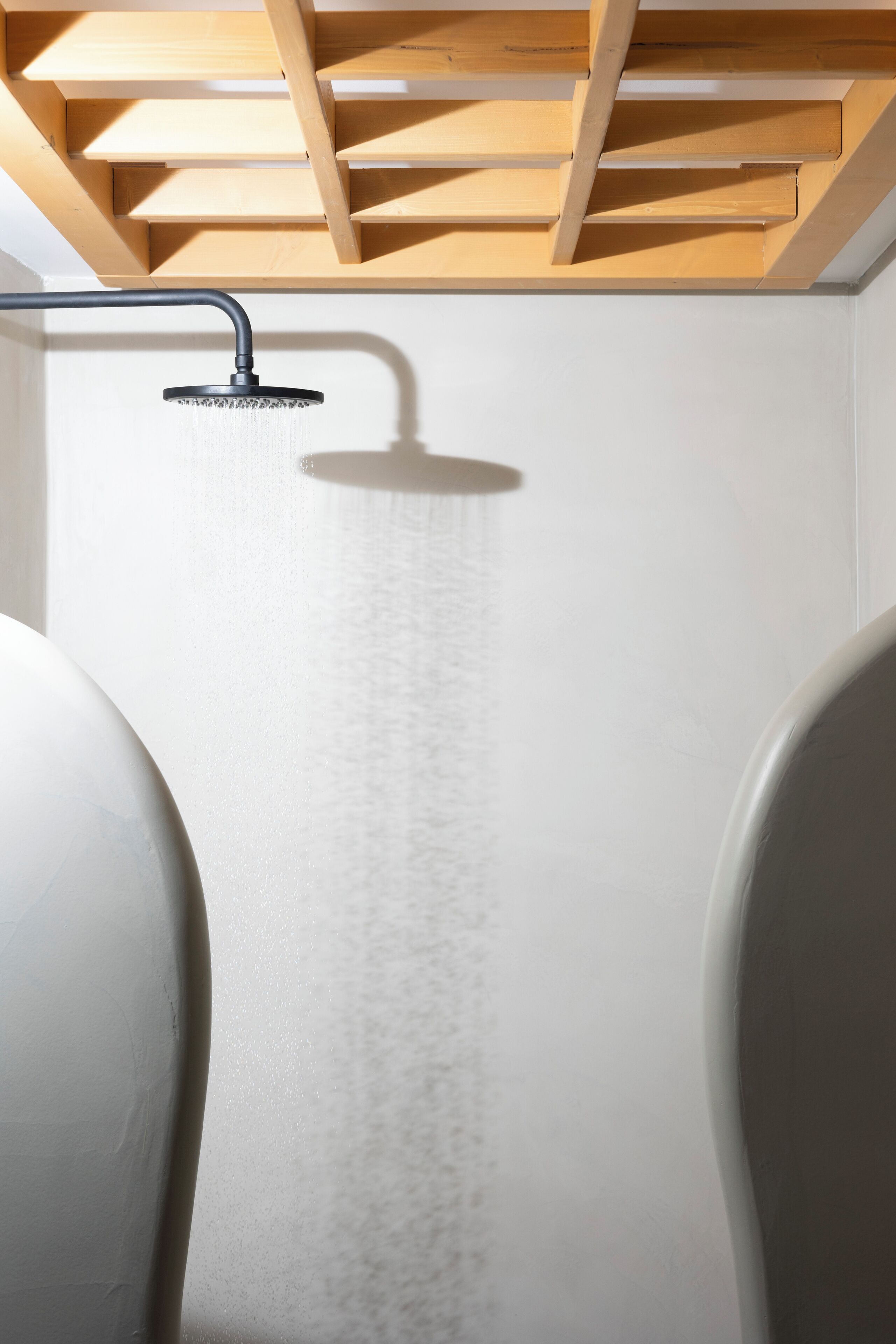 A shower with a wooden ceiling structure, a white wall, and a bathtub.