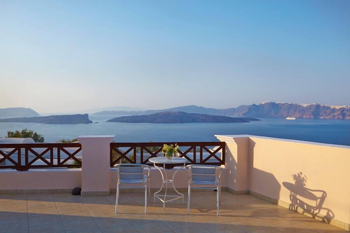 A terrace with two white chairs and a table, overlooking a scenic view of a coastline and mountains.