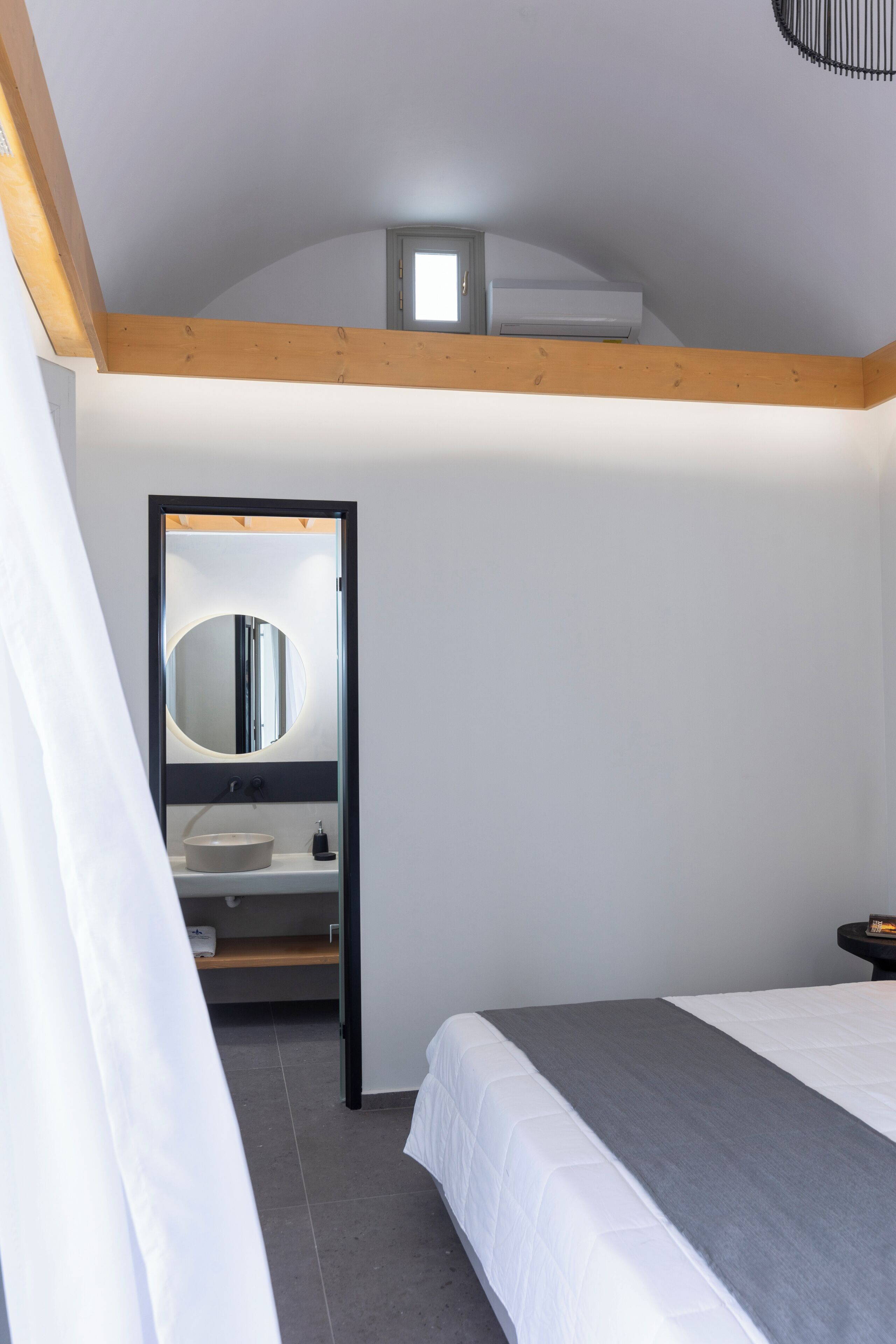A bedroom with a bed, a bedside table, a mirror, and a built-in air conditioning unit above the bed.