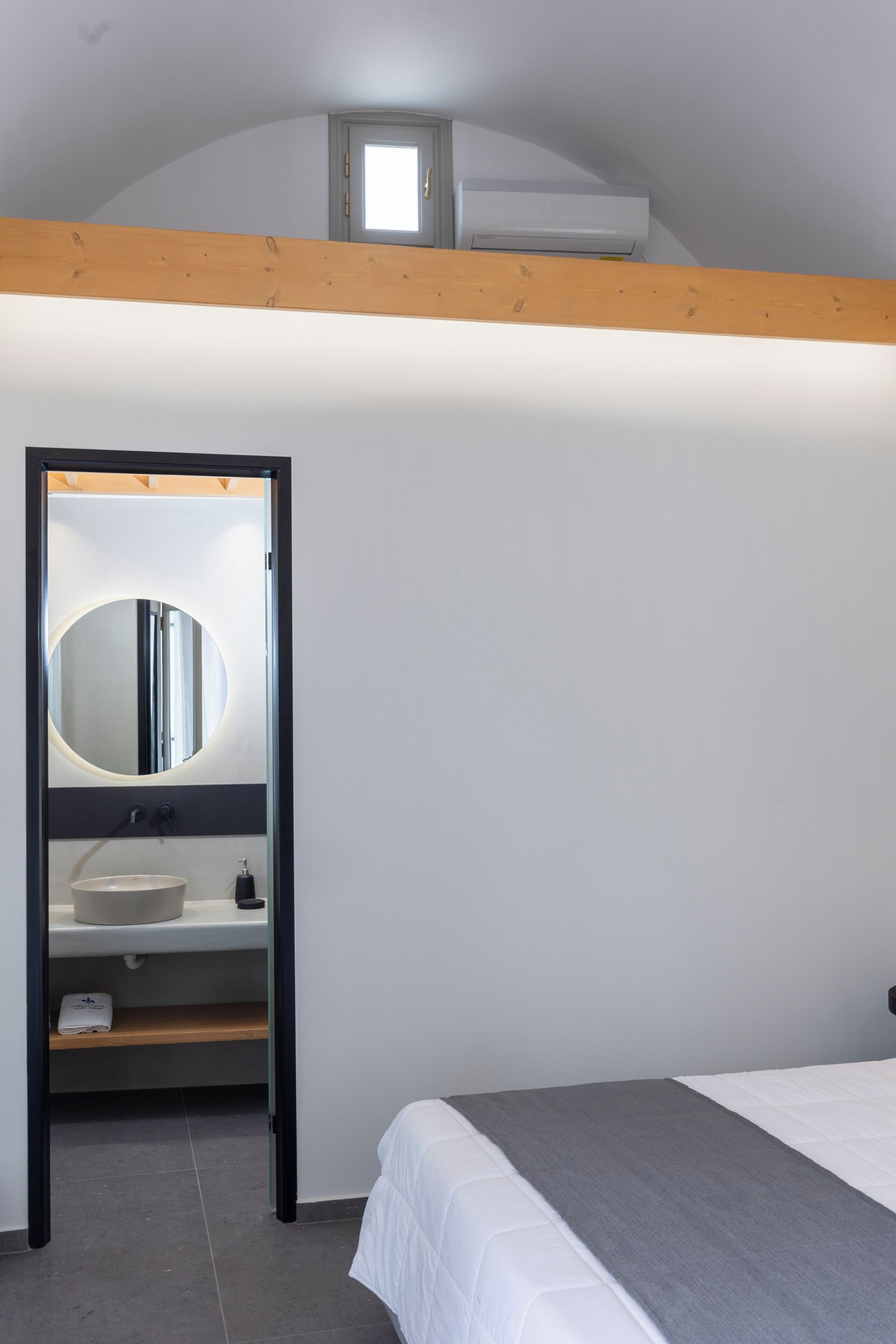 Un dormitorio con una cama litera, un espejo redondo, un lavabo y una ventana sobre la cama.