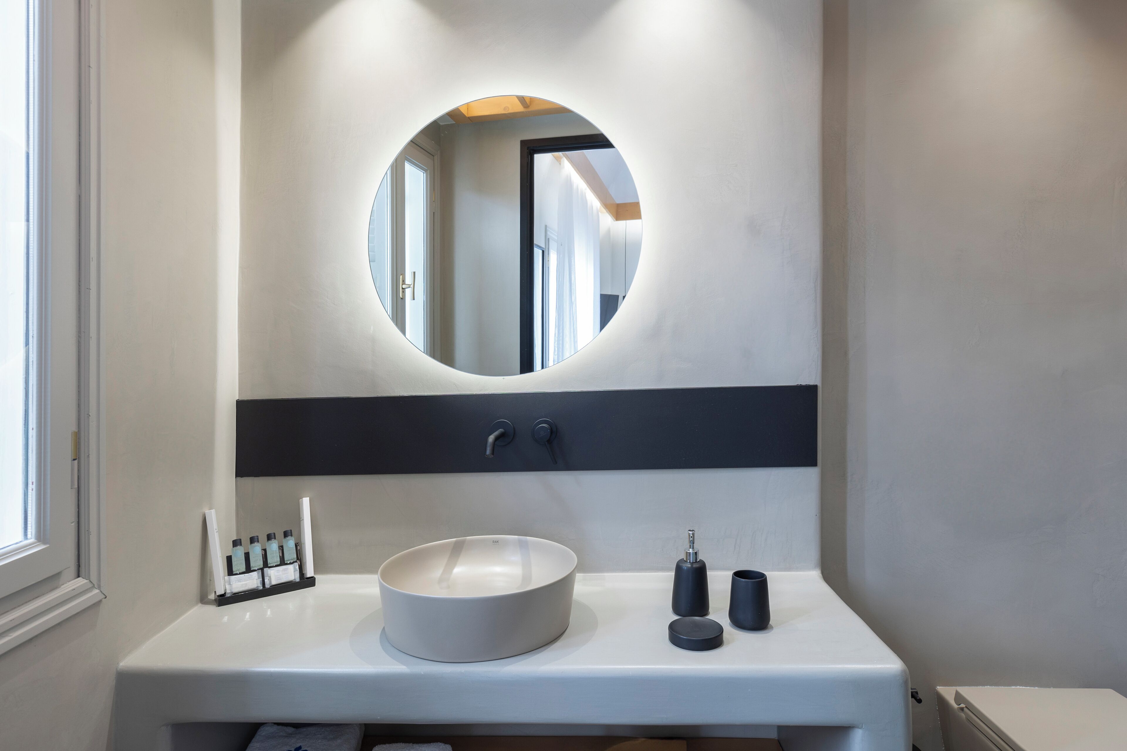 Un baño moderno con un espejo redondo, un lavabo blanco y una encimera negra.