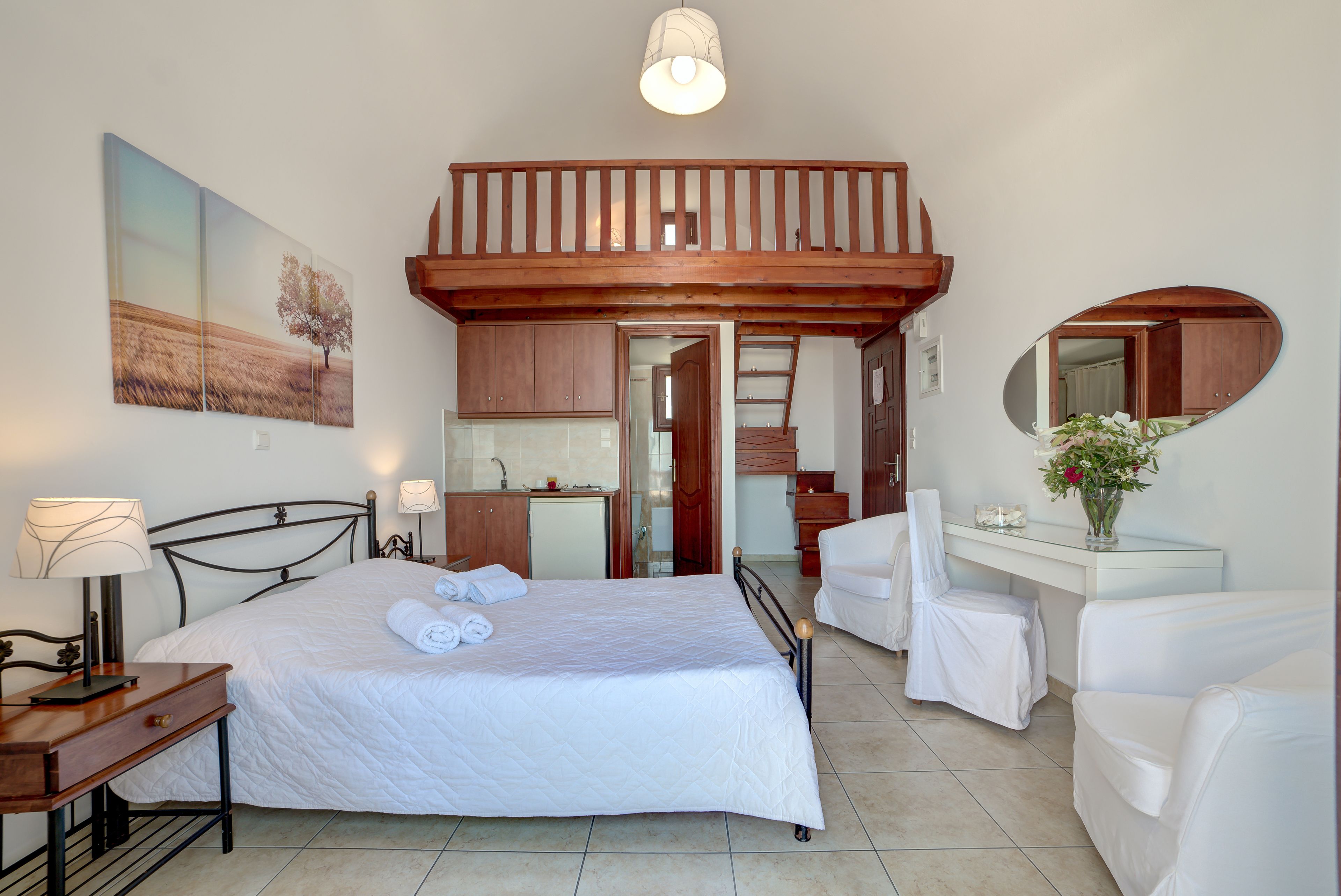 A bedroom with a bed, bedside tables, a desk, a chair, a mirror, and a balcony.