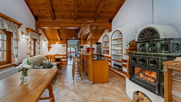 Una cocina acogedora con un estufa de leña, un comedor con una mesa larga y una barra con estantes llenos de botellas.