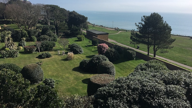 A landscaped garden with manicured lawns, hedges, and trees, leading to a body of water. - Hotel Riviera (Bournemouth)
