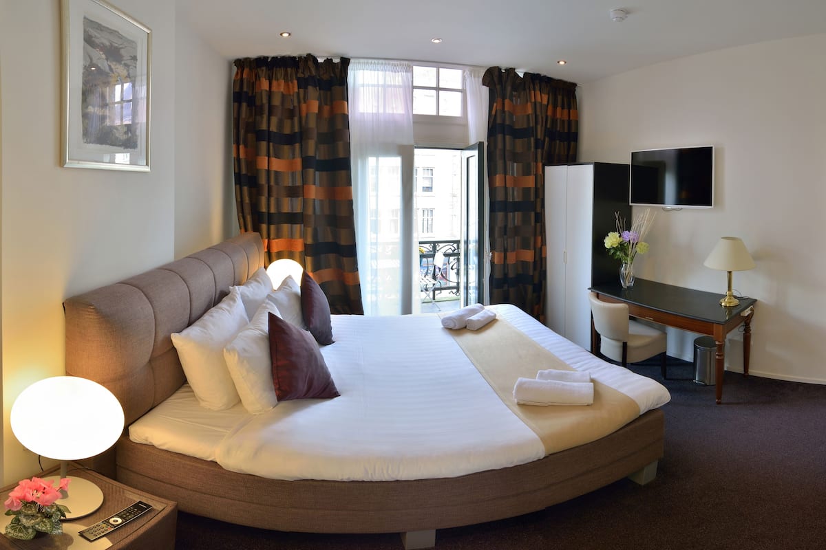 Una habitación de hotel con una cama grande, un escritorio, un televisor y una ventana con cortinas.