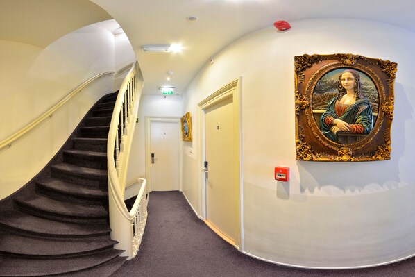 A hallway with a spiral staircase, a framed artwork on the wall, and a door with the number 13.