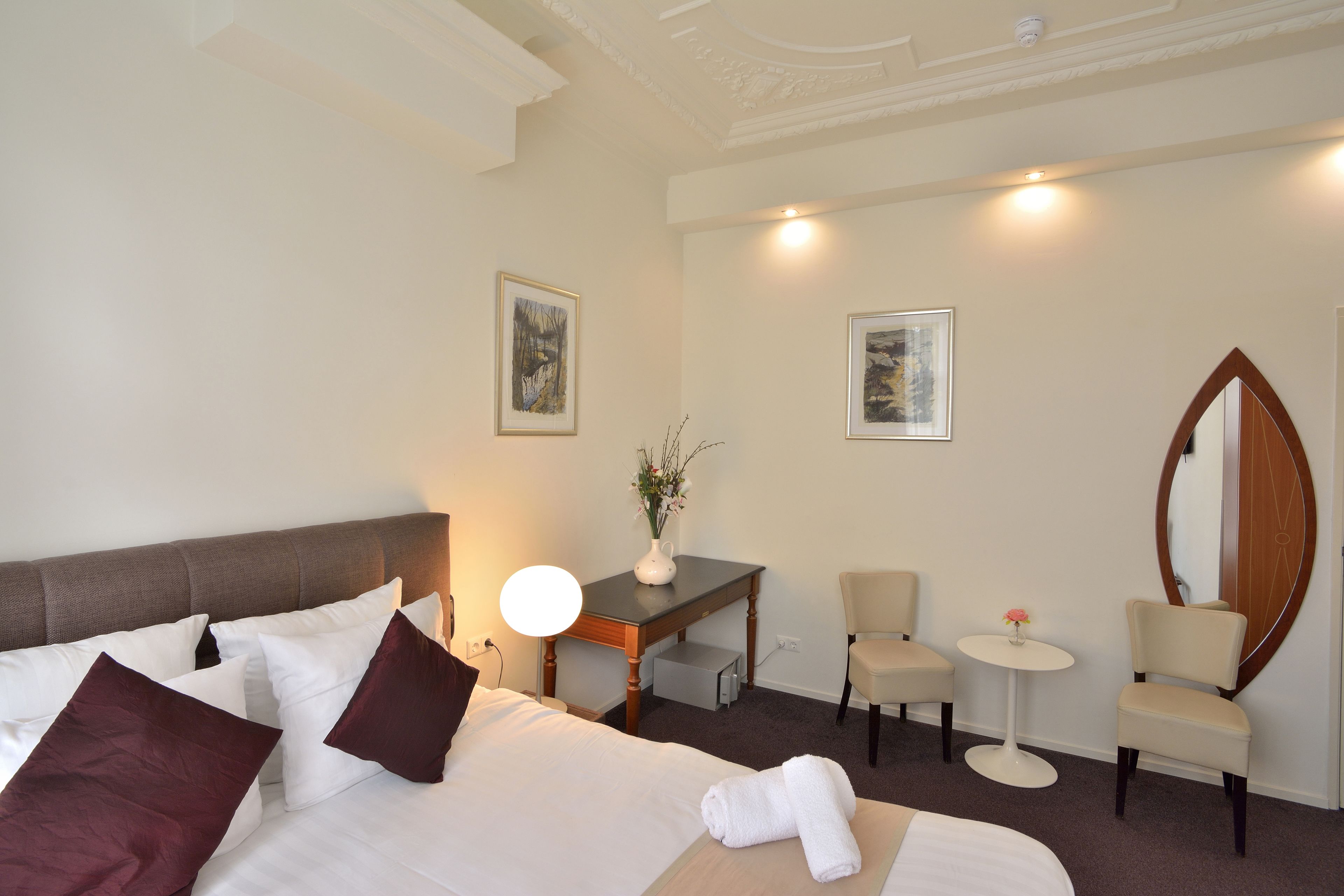 A hotel room with a bed, a desk, two chairs, a small table, and a mirror.