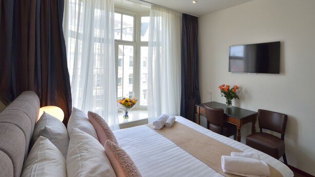 A hotel room with a bed, a desk, a chair, a TV, and a window with curtains.