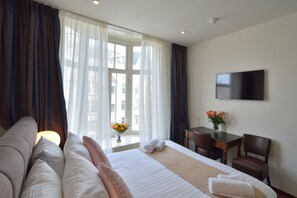Une chambre d’hôtel avec un lit, un bureau, une chaise, une télévision et une fenêtre avec des rideaux.