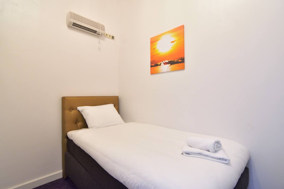 Una cama individual con colchón blanco y cabecera marrón en una habitación de hotel.