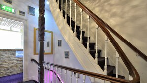 A staircase with white balusters and a wooden handrail, leading to a room with a stone wall and a sign indicating a hotel.