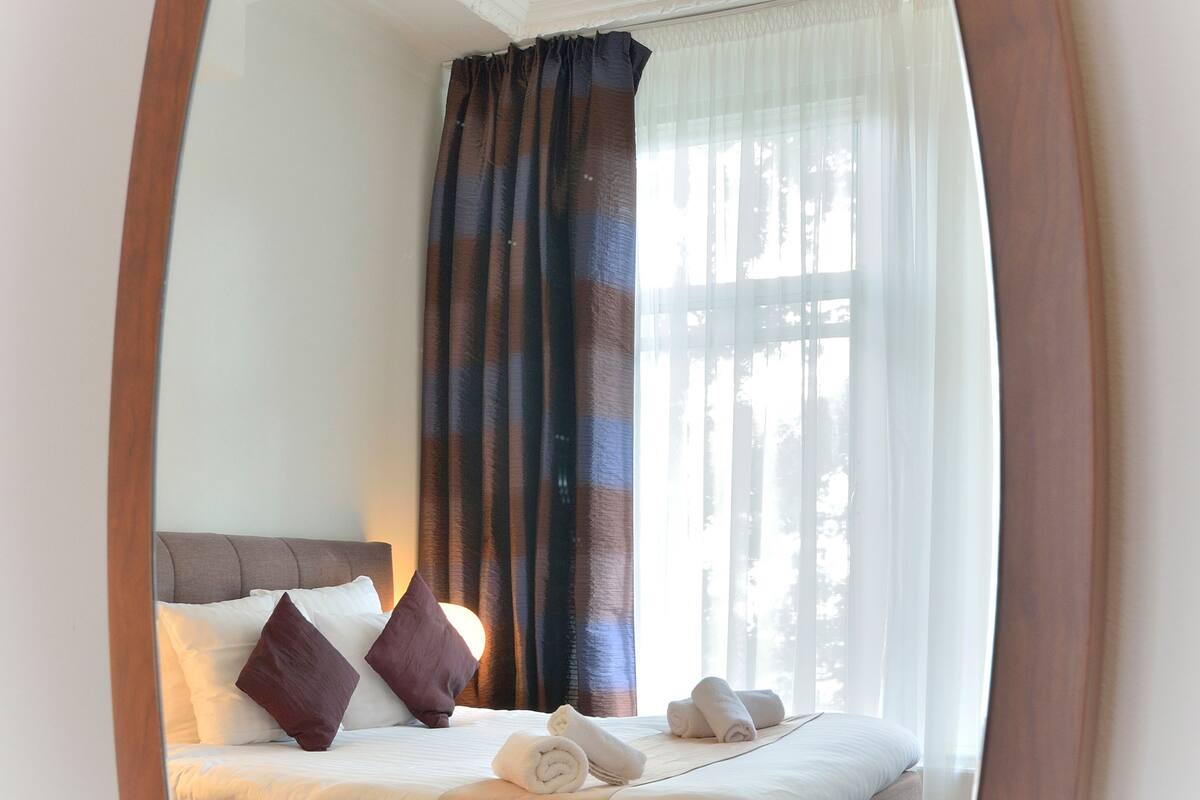 Un dormitorio con cama, almohadas, teléfono y ventana con cortinas.